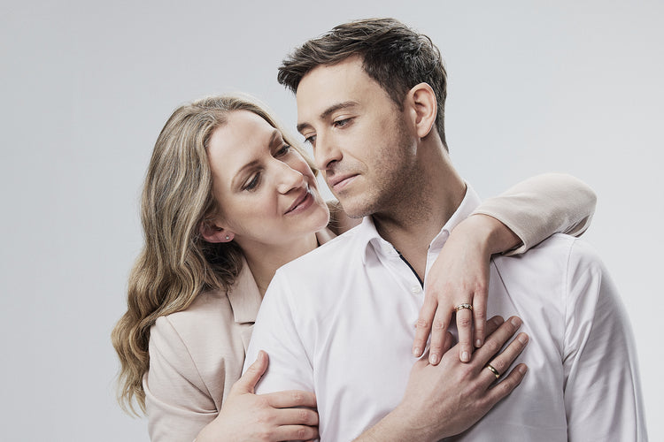 Romantisches Paar in inniger Umarmung in eleganten beigen Outfits - beide tragen passende goldene Eheringe 