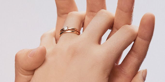 Paar verschränkt Hände, Ehering und Solitär-Ring in Rotgold an Damenhand
