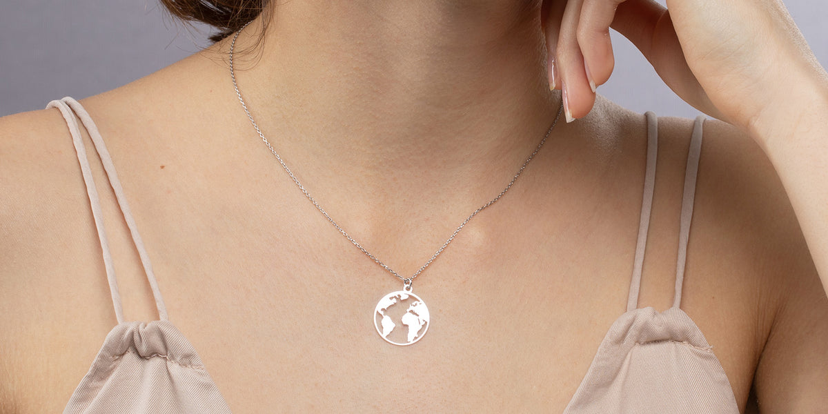 Frau trägt silberne Halskette mit rundem Weltkarten-Anhänger zu einem beigen Trägerkleid - symbolischer Schmuck